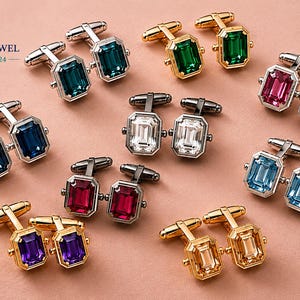 May include: A collection of cufflinks in various colors, including teal, blue, green, pink, clear, and purple. The cufflinks have a rectangular gemstone design and are set in silver or gold-toned metal. The image includes the text "Peacock Jewel Collection 24".
