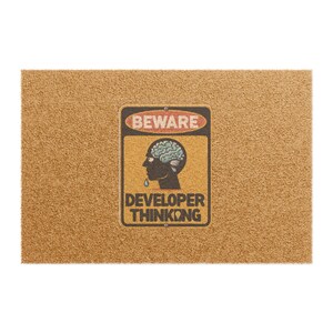May include: A rectangular doormat with a textured, tan surface. A distressed sign with the word "BEWARE" at the top and "DEVELOPER THINKING" at the bottom is centered. The sign features a brain graphic.