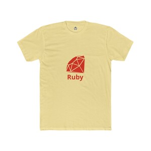 Op de afbeelding: Lichtgele t-shirt met een rood geometrisch robijnontwerp en het woord "Ruby" eronder. Het shirt heeft korte mouwen en een ronde hals.