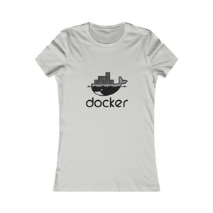 Op de afbeelding: Lichtgrijs t-shirt met een zwart-witte afbeelding van een walvis die gestapelde containers draagt, met het woord "docker" eronder. Het shirt heeft korte mouwen en een ronde hals.