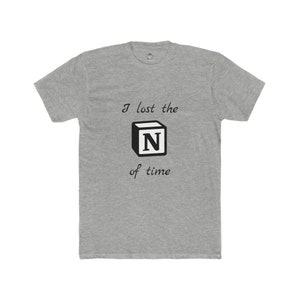 May include: A heather gray t-shirt with the text "I lost the N of time" in black. The letter "N" is inside a black cube. The shirt has short sleeves and a crew neck.