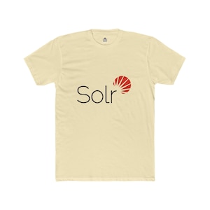 以下が含まれることがあります： 黒い「Solr」の文字と赤と白のサンバーストグラフィックが特徴のクリーム色のTシャツ。半袖、クルーネックのシャツで、デザインは前面にプリントされています。