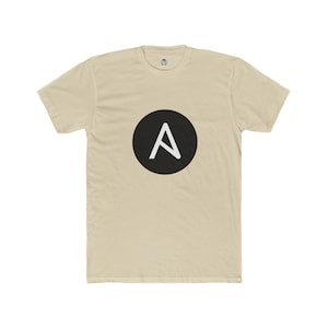 May include: A beige t-shirt with a black circular design containing a white letter 'A'. The t-shirt has a crew neck and short sleeves. The graphic is positioned centrally on the front of the garment.