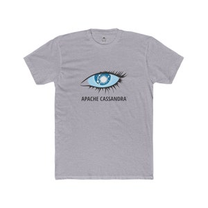 May include: A light gray t-shirt featuring a stylized eye design with blue and white accents. The text "APACHE CASSANDRA" is printed below the eye. The shirt has short sleeves and a crew neck.