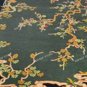 May include: Dark green area rug with a floral design featuring branches with yellow, orange, and red flowers. The rug has a black border and a stylized cloud-like pattern at the bottom. The words "RAFRAF STORE" are printed on the rug.