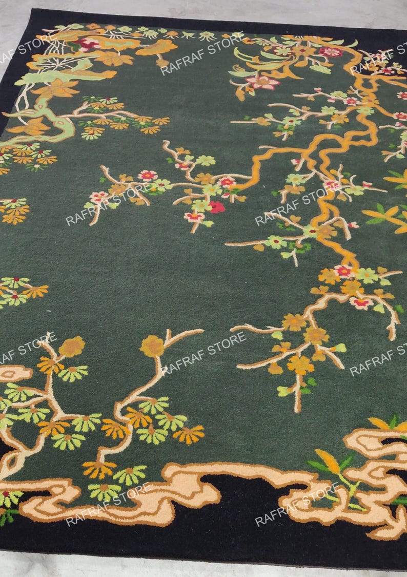 May include: Dark green area rug with a floral design featuring branches with yellow, orange, and red flowers. The rug has a black border and a stylized cloud-like pattern at the bottom. The words "RAFRAF STORE" are printed on the rug.