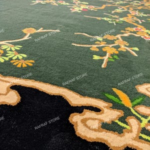 May include: A large, dark green rug with a floral design. The rug features branches with yellow and orange flowers and leaves. The border is black with a tan-coloured design. The text "RAFRAF STORE" is printed on the rug.