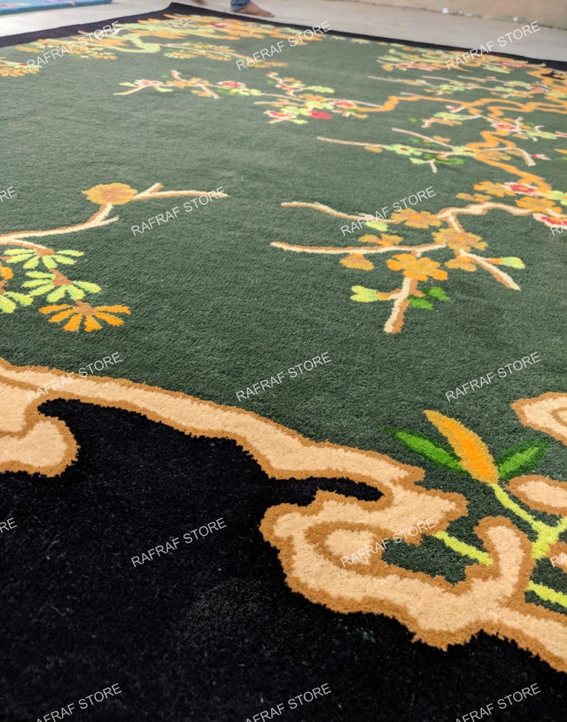 May include: A large, dark green rug with a floral design. The rug features branches with yellow and orange flowers and leaves. The border is black with a tan-coloured design. The text "RAFRAF STORE" is printed on the rug.