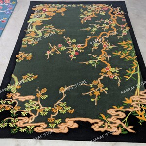 May include: A dark green rectangular rug with a black border. The rug features an intricate floral design with branches, leaves, and flowers in shades of orange, yellow, and green. The design is set against a dark green background.