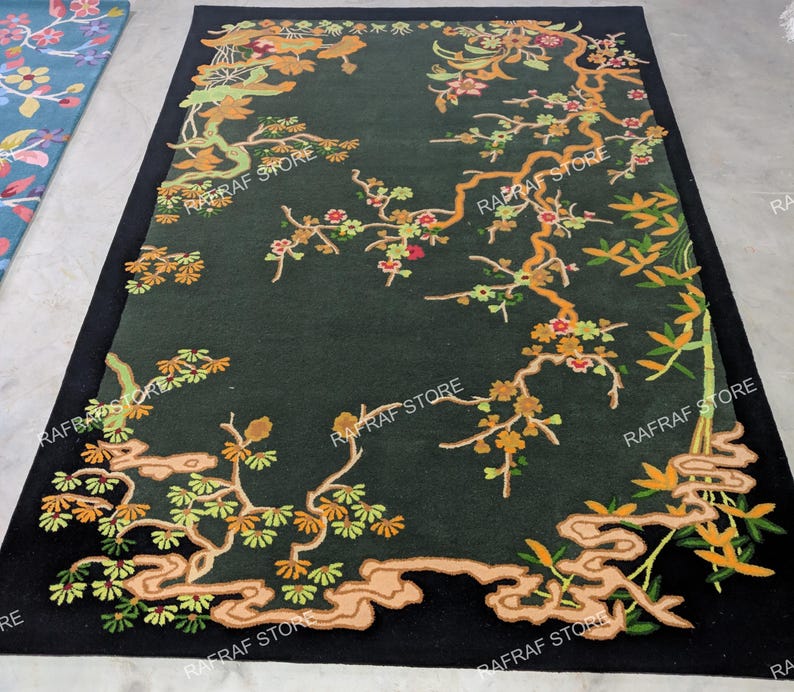 May include: A dark green rectangular rug with a black border. The rug features an intricate floral design with branches, leaves, and flowers in shades of orange, yellow, and green. The design is set against a dark green background.