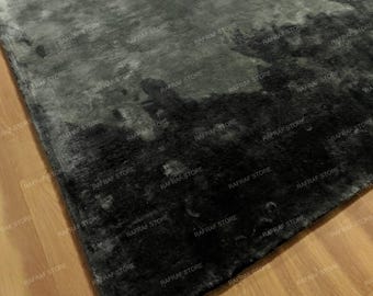 May include: A dark gray area rug with a textured, plush surface. The rug has a gradient effect, transitioning from lighter gray to deep black. The rug is on a wooden floor.