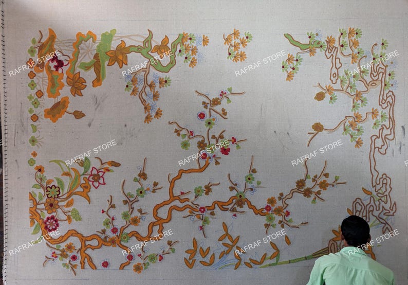 May include: An off-white textile with an embroidered floral pattern in orange, green, and red. The design includes branches, flowers, and leaves. The words "RAFRAF STORE" are printed on the textile.