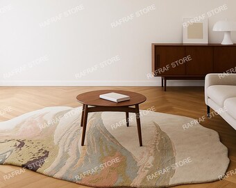 May include: A modern living room scene featuring a round wooden coffee table with a book, a beige sofa, and a unique, abstract-shaped rug with muted colors. A wooden cabinet and a lamp are also visible.