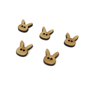 Puede incluir: Cinco botones de madera con forma de conejos pintados de marrón. Cada botón tiene dos puntos negros para los ojos.