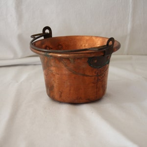 May include: A small copper pot with a handle. The pot has a hammered finish and is slightly tarnished.