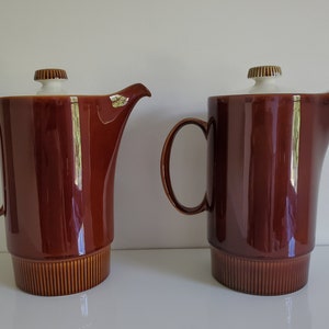 May include: Two brown ceramic coffee pots with white lids and gold accents. The pots have a ribbed design around the bottom.