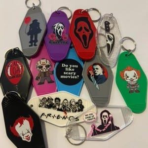 May include: A collection of novelty keychains featuring horror movie characters and quotes. Designs include Pennywise, Ghostface, Jason Voorhees, and the Friends logo. Keychains are various colors and shapes.