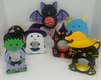 May include: A collection of Halloween-themed paper cutouts. The cutouts include a black bat with purple wings, a green Frankenstein's monster, a white ghost, a black cat with a witch hat, a blue monster, and a haunted house.