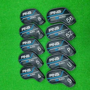 May include: A collection of black PING G440 golf club head covers. Each cover has a white and blue design with a number or letter indicating the club. The covers are arranged on a green surface.