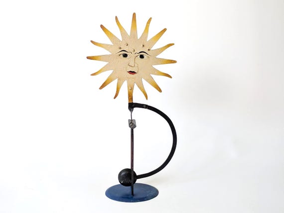 An Art Deco sun-face pendulum that uses anamorphic illusion so the face only 'appears' as it swings — genuinely trippy kinetic trick.