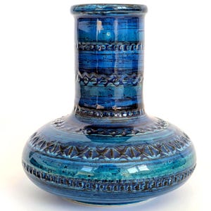 Op de afbeelding: Een blauwe keramische vaas met een bolvormige basis en een cilindrische hals. De vaas heeft een gestructureerd oppervlak met horizontale banden en geometrische patronen in blauw- en tinten. De vaas is ongeveer 25 cm hoog.