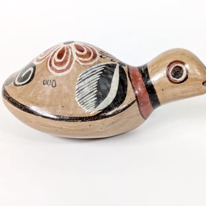 May include: Hand-painted ceramic bird figurine in tan, with black, white, and red accents. The bird has a rounded body and a long, slender neck. The body is decorated with floral and geometric patterns. The figurine is approximately 15 cm long.