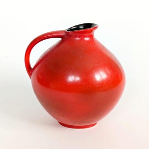 Peut inclure: Pichet en céramique rouge vif avec un corps arrondi et une anse incurvée. L'intérieur de l'ouverture est noir. Le pichet est de couleur unie et a une finition brillante. Objet décoratif.