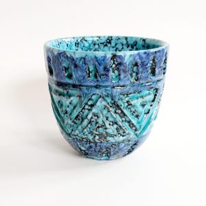 Può includere: Un vaso in ceramica con una superficie strutturata e una vivace combinazione di colori blu e turchese. Il vaso presenta un motivo geometrico e una finitura maculata, che aggiunge interesse visivo. Il design ricorda la ceramica vintage.