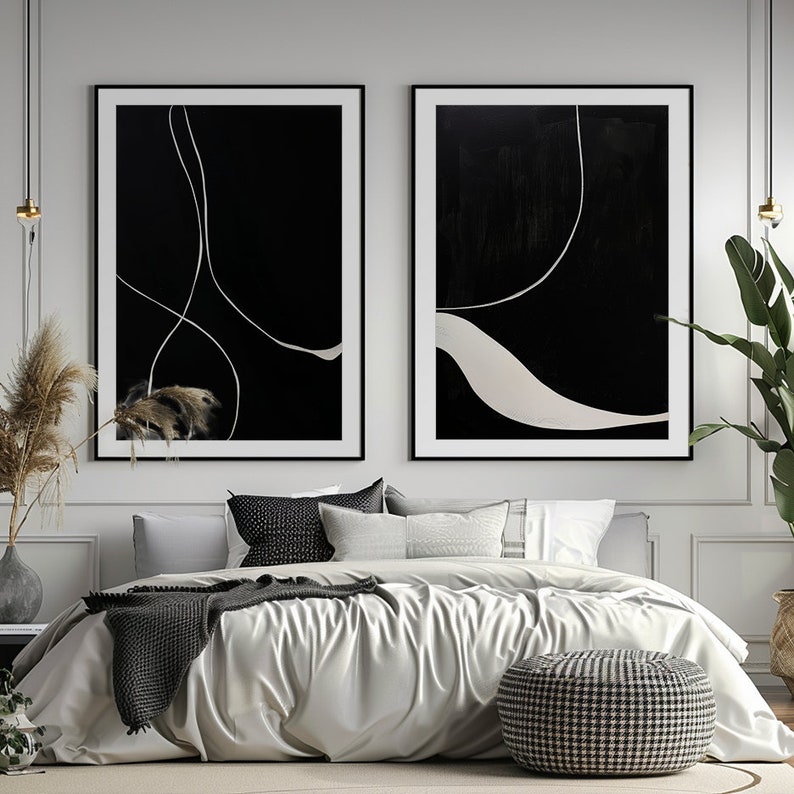 K&ouml;nnte beinhalten: Zwei gerahmte abstrakte Kunstwerke. Jedes hat einen schwarzen Hintergrund mit wei&szlig;en, geschwungenen Linien. Die Kunstwerke werden &uuml;ber einem Bett mit einer wei&szlig;en Bettdecke, grauen Kissen und einem gemusterten Hocker ausgestellt. Der Raum ist mit Pflanzen und neutralen T&ouml;nen dekoriert.