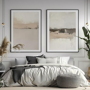 Puede incluir: Dos pinturas abstractas de paisajes en marcos negros, colgadas sobre una cama blanca con una manta gris y almohadas con estampado en blanco y negro.