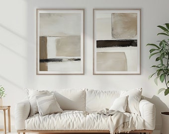 May include: Two abstract paintings in beige, brown, and black frames, hanging on a white wall above a white sofa with a throw blanket.