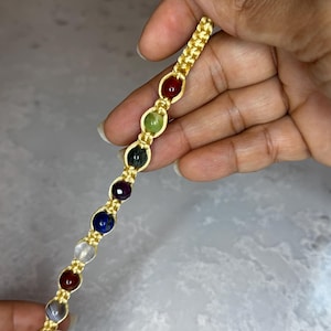 May include: Gold-toned bracelet featuring a series of colorful gemstones. The bracelet has a chain-like design with oval-shaped links holding the stones. The gemstones are in various colors, including red, green, blue, and clear.