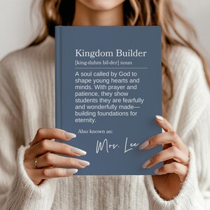 May include: A navy blue journal with the words "Kingdom Builder" and a definition printed on the cover. The journal also includes the text "Mrs. Lee" in cursive.