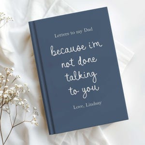 May include: A dark blue hardcover journal with white text that reads Letters to my Dad, because I'm not done talking to you, and Love, Lindsay. The book cover features a clean, minimalist design with a mix of serif and handwritten script fonts.
