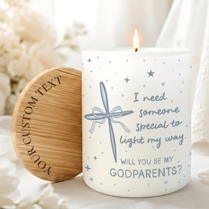May include: A white cylindrical candle with a lit wick, featuring a blue cross graphic, star accents, and the text: I need someone special to light my way. WILL YOU BE MY GODPARENTS? A round bamboo lid with the engraved text YOUR CUSTOM TEXT is adjacent.
