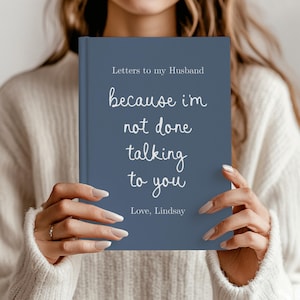 May include: A slate blue hardback journal with white text that reads Letters to my Husband, because i'm not done talking to you, and Love, Lindsay. The book features a clean, solid-coloured cover with a mix of serif and script typography.