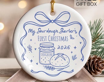 May include: A round white ceramic ornament featuring a blue line drawing of a jar labeled Doughlene, a loaf of bread, and the text My Sourdough Starter's First Christmas 2026. The ornament is topped with a gold string for hanging.