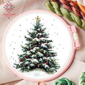 May include: A cross stitch pattern of a snowy Christmas tree with red baubles and a gold star on top. The tree is surrounded by a white background with a light dusting of snow.