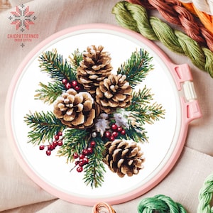 May include: A cross stitch pattern featuring a wintery scene with pine branches, pine cones, and red berries. The design is framed in a pink embroidery hoop.