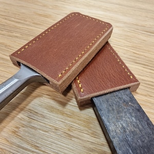 May include: Two brown leather sheaths with yellow stitching, one is covering a metal chisel, the other is covering a metal blade.