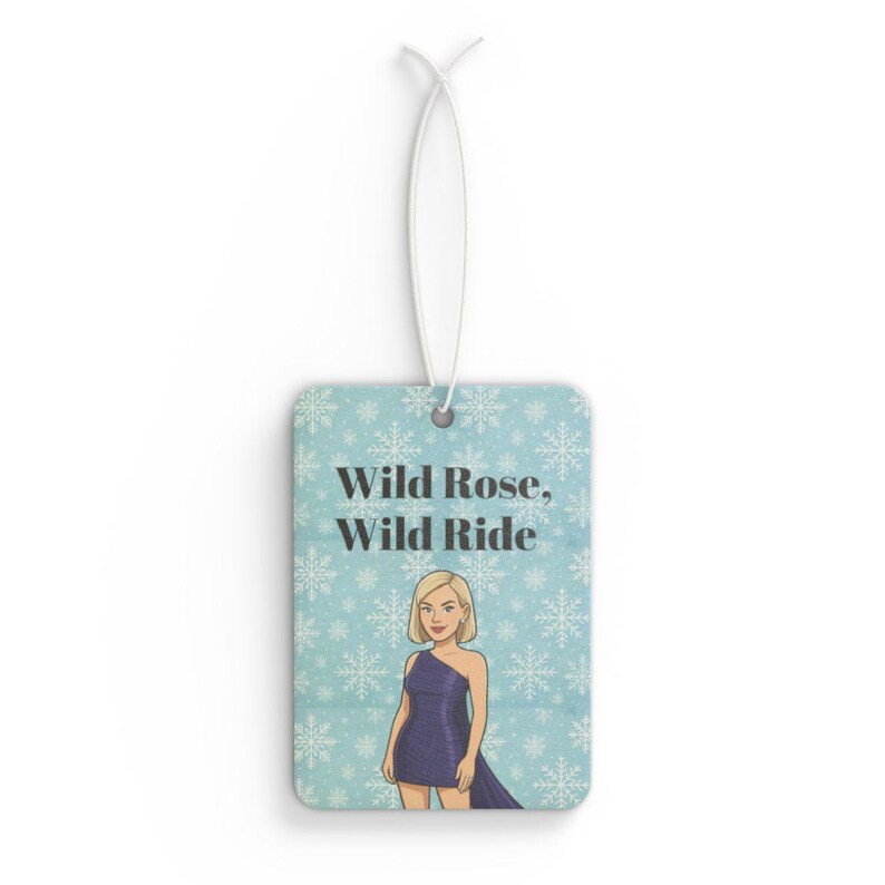 May include: Rectangular air freshener with a light blue background and a snowflake pattern. The air freshener features the text "Wild Rose, Wild Ride" and an illustration of a woman in a purple dress. A white string is attached for hanging.