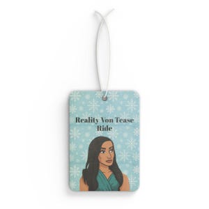 May include: Rectangular air freshener with a light blue background and a snowflake pattern. The air freshener features an illustration of a woman and the text "Reality Von Tease Ride". A white string is attached for hanging.