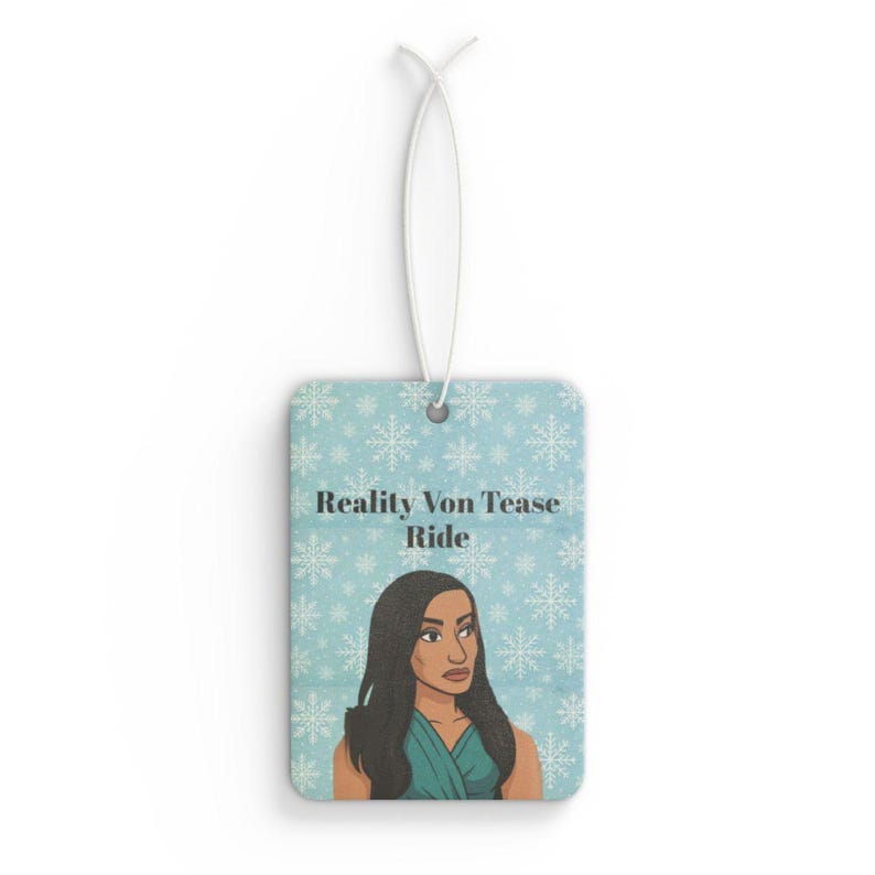 May include: Rectangular air freshener with a light blue background and a snowflake pattern. The air freshener features an illustration of a woman and the text "Reality Von Tease Ride". A white string is attached for hanging.