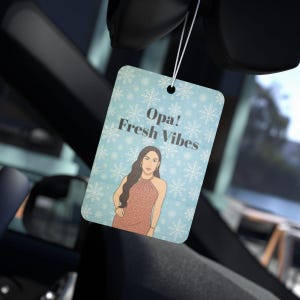May include: A rectangular car air freshener with a light blue background and white snowflake pattern. The text "Opa! Fresh Vibes" is displayed above an illustration of a woman in a pink dress.