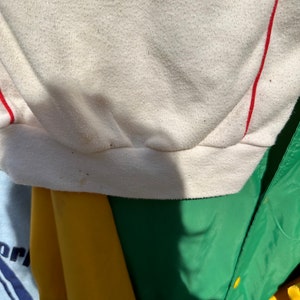 May include: Close-up of the bottom edge of a white sweatshirt with red stripes. The fabric is textured and has a slight sheen.