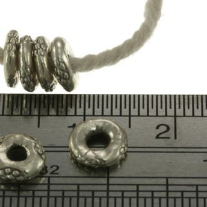May include: Four silver-toned metal beads with a textured surface are threaded on a white string. Two additional matching beads are placed on a metal ruler, showing a diameter of approximately 1.3 cm for each individual round bead.