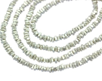 May include: Close-up of four strands of silver-colored beaded necklaces. The beads are small, irregular, and faceted, giving them a textured appearance. The necklaces are displayed against a white background, highlighting the metallic sheen of the beads.