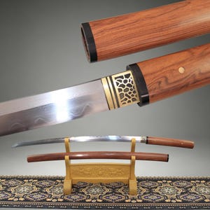 May include: A Japanese-style sword with a curved steel blade featuring a visible folded metal pattern. The handle and scabbard are crafted from polished wood with black accents and a gold-colored metal collar with a cutout geometric design.