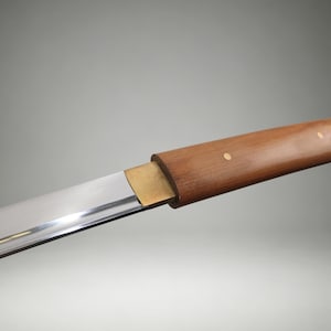 May include: A straight, polished steel blade attached to a smooth, cylindrical wooden handle. A rectangular brass bolster connects the blade to the handle, which features two small, circular brass rivets embedded in the wood grain surface.