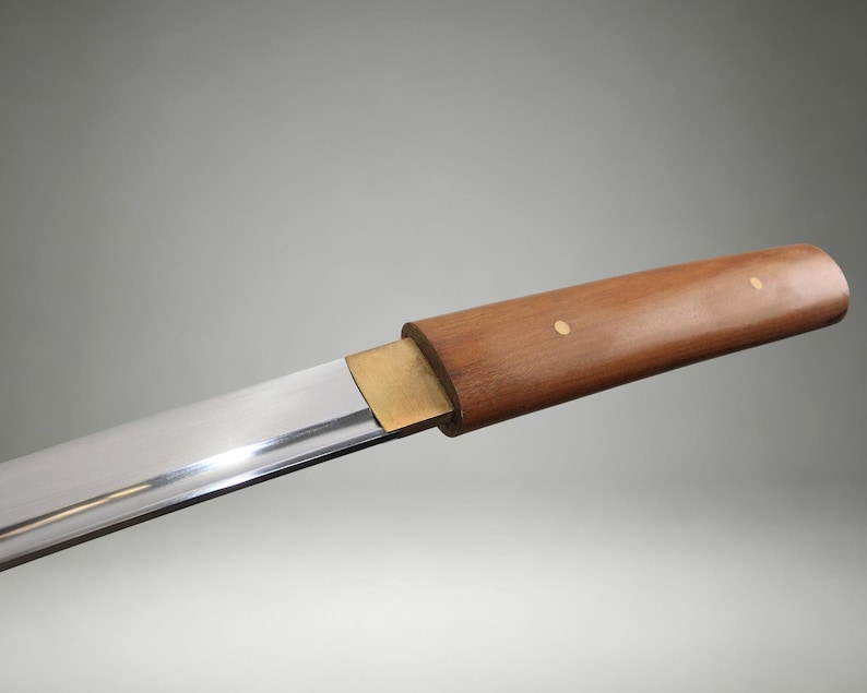 May include: A straight, polished steel blade attached to a smooth, cylindrical wooden handle. A rectangular brass bolster connects the blade to the handle, which features two small, circular brass rivets embedded in the wood grain surface.